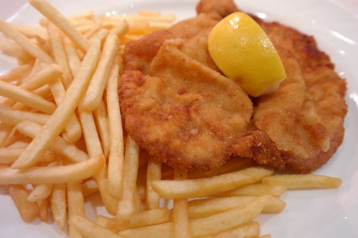 Paniertes Putenschnitzel mit Pommes und Zitrone auf einem Teller angerichtet